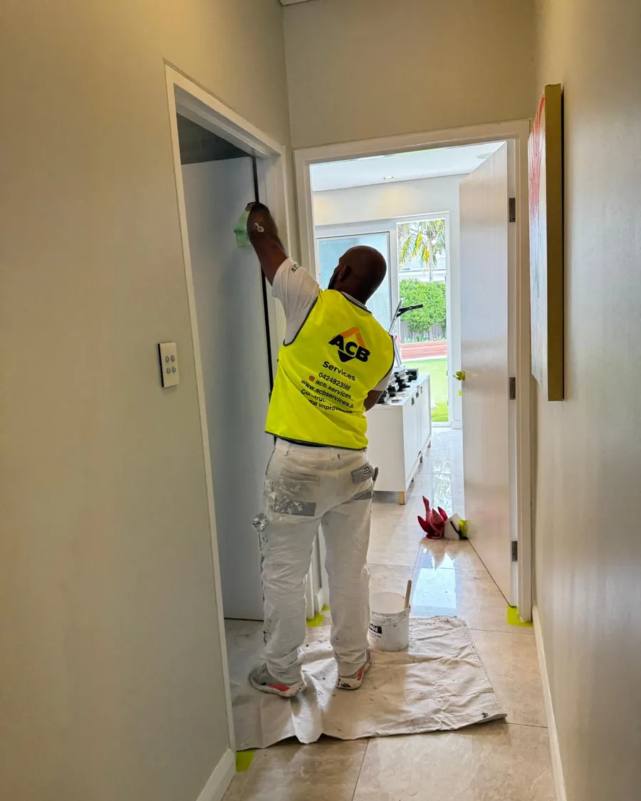 ACB painter in a hi-vis vest cutting in a door frame